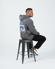 Grey BJJ hoodie seated side profile lifestyle shot with adult male model on stool showing relaxed drape