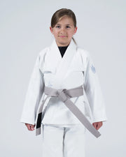 A young girl wearing a white martial arts gi with a gray belt, standing against a light gray studio background.
