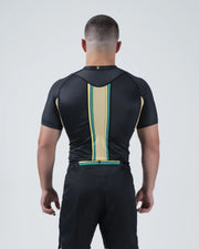 Kingz Player Special Limited Edition Rashguard Black Gold - Upper Body Back Detail View Male Athlete Short Sleeve Gold Champagne Center Stripe Teal Green Border Lotus JPS F1 Inspired [color:Black]