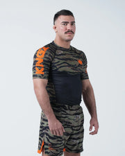 Kingz Always Hunting Rashguard Green Camo - Full Body 3/4 Angled View Left Side Male Athlete Short Sleeve Tiger Camo Orange Crown Logo Large KINGZ Text Sleeve Camo Shorts