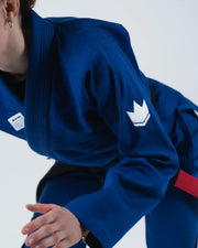 Kingz Kore V2 Women's Jiu Jitsu Gi Blue - Close-Up Action View Female Athlete Blue Gi White Crown Badge Left Arm Red Belt Detail Durable Weave BJJ Training Gi [color:Blue]