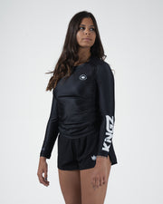 Kingz Kore V2 Long Sleeve Rashguard Black - Full Body 3/4 Front Right Side View Female Athlete Long Sleeve Black Body KINGZ Bold White Vertical Right Sleeve Text Crown Logo Circle Chest Matching Black Shorts Women's BJJ Kore Collection