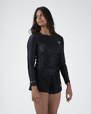 Kingz Kore V2 Long Sleeve Rashguard Black - Full Body 3/4 Front Left Side View Female Athlete Long Sleeve All Black Body Crown Logo Circle Chest KINGZ KIMONOS EST 2011 White Left Sleeve Text Matching Black Shorts BJJ Women's No-Gi Kore