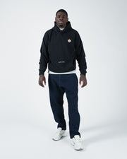 Black BJJ hoodie full body walking lifestyle shot with adult male model in jeans and white sneakers