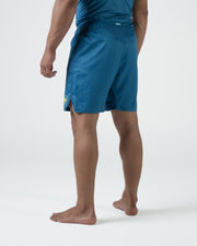 Kingz MI-K Roots Shorts Blue - Full Body Left-Back Side Profile Male Athlete Steel Blue Teal MI-K Badge Gold Right Lower Leg Competition Cut Men's Grappling Shorts No-Gi BJJ MI-K Roots Limited Edition