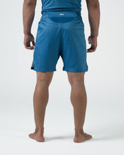 Kingz MI-K Roots Shorts Blue - Full Body Left-Back Side Profile Alternate Stance Male Athlete Steel Blue Teal Gold Badge Right Leg Side Split Competition Cut Men's Grappling Shorts No-Gi BJJ