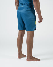 Kingz MI-K Roots Shorts Blue - Full Body Left Side Profile Male Athlete Steel Blue KINGZ Gold Vertical Text Left Leg MI-K Waistband Text Side Split Competition Cut Men's Grappling Shorts No-Gi BJJ