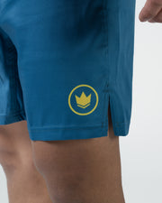 Kingz MI-K Roots Shorts Blue - Close Up Badge Detail MI-K Gold Crown Circular Badge Right Thigh Gold Crown with Horizontal Stripes in Gold Circle Steel Blue Fabric Side Split Visible Men's Grappling Shorts No-Gi BJJ MI-K Roots Mica Galvao