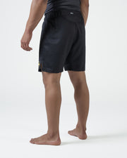 Kingz MI-K Roots Onça Pintada Shorts Black - Full Body Left-Back Side Profile Male Athlete Dark Charcoal MI-K Waistband Text Gold Badge Right Leg Competition Cut Men's Grappling Shorts No-Gi BJJ