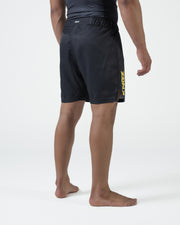 Kingz MI-K Roots Onça Pintada Shorts Black - Full Body Left Side Profile Male Athlete Dark Charcoal KINGZ Gold Vertical Text Left Leg Side Split Men's Grappling Shorts No-Gi BJJ
