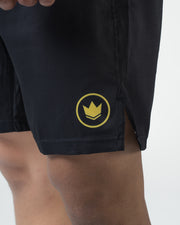 Kingz MI-K Roots Onça Pintada Shorts Black - Close Up Badge Detail MI-K Gold Crown Circular Badge Right Thigh Dark Charcoal Black Fabric Side Split Visible Men's Grappling Shorts No-Gi BJJ MI-K Roots Jaguar Collection