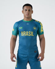 Kingz MI-K Roots Rashguard Teal Blue - Full Body Front View Male Athlete Short Sleeve BRASIL Yellow Text Brazil Flag Crown Logo Green Collar Teal Blue Matching Shorts Limited Edition BJJ