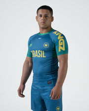 Kingz MI-K Roots Rashguard Teal Blue - Full Body 3/4 Angled Front View Male Athlete Short Sleeve BRASIL Large Yellow Text Brazil Flag Crown Logo Green Cuffs Collar Teal Blue Shorts