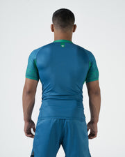 Kingz MI-K Roots Rashguard Teal Blue - Full Body Straight Back View Male Athlete Short Sleeve Crown Logo Upper Back Green Patterned Cuffs Teal Blue Back Panel Shorts Brazilian Limited Edition