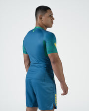 Kingz MI-K Roots Rashguard Teal Blue - Full Body 3/4 Back View Right Side Male Athlete Short Sleeve Green Tribal Pattern Sleeves Crown Logo Teal Blue Shorts KINGZ Text Brazilian Inspired