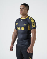 Kingz MI-K Roots Onça Pintada Rashguard Midnight Gray - Full Body 3/4 Angled Front View Male Athlete Short Sleeve BRASIL Gold Text Brazil Flag Crown Logo Gold Collar KINGZ Text Side
