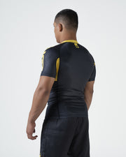 Kingz MI-K Roots Onça Pintada Rashguard Midnight Gray - Full Body Straight Front View Barefoot Male Athlete Short Sleeve BRASIL Gold Text Brazil Flag Crown Logo Dark Gray Shorts Jaguar Pattern