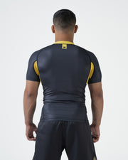 Kingz MI-K Roots Onça Pintada Rashguard Midnight Gray - Full Body Front View Barefoot Male Athlete Short Sleeve Jaguar Pattern BRASIL Gold Text Crown Logo Gold Collar Dark Gray Shorts BJJ