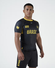 Kingz MI-K Roots Onça Pintada Rashguard Midnight Gray - Full Body Angled Front View Male Athlete Short Sleeve BRASIL Bold Gold Text Brazil Flag Crown Rank Logos Gold Collar Gold Side Panel