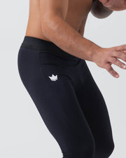 Kingz Kore Grappling Spats Black - Action Close Up Waist-to-Knee View Shirtless Male Athlete Dynamic Grappling Pose Large White Crown Logo Left Thigh All-Black Men's No-Gi BJJ Spats Kore Collection Crown Logo Detail
